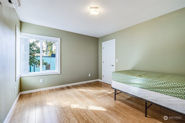 unfurnished bedroom with an AC wall unit and light wood-type flooring