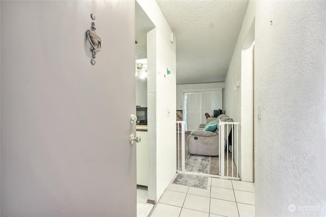 corridor with a textured wall, a textured ceiling, and light tile patterned floors