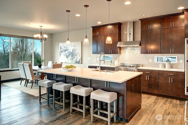 kitchen featuring sink, wall chimney exhaust hood, light hardwood / wood-style flooring, an island with sink, and decorative light fixtures