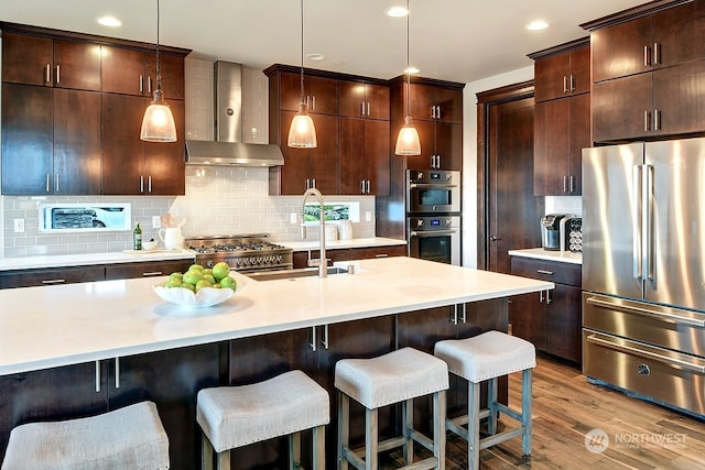 kitchen featuring appliances with stainless steel finishes, light wood-type flooring, pendant lighting, and wall chimney range hood