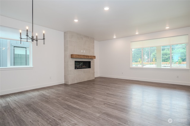 unfurnished living room featuring a notable chandelier, a tiled fireplace, and dark hardwood / wood-style flooring