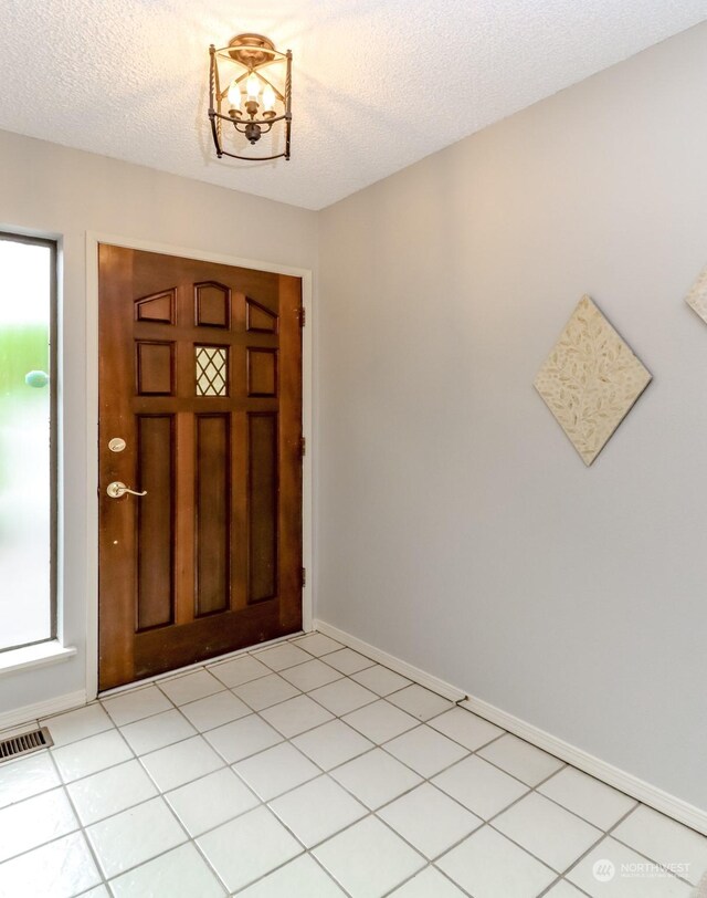 tiled entrance foyer featuring a notable chandelier and a textured ceiling