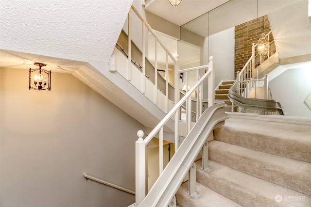 stairs featuring a textured ceiling, a chandelier, and brick wall