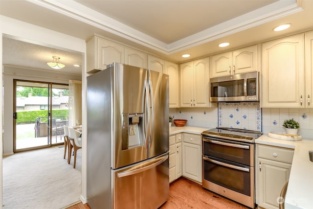 kitchen with decorative backsplash, a raised ceiling, light colored carpet, crown molding, and stainless steel appliances