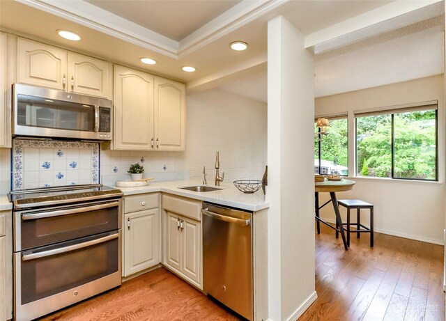 kitchen featuring backsplash, sink, light wood-type flooring, a raised ceiling, and stainless steel appliances