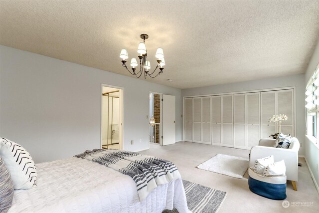 carpeted bedroom featuring a closet, a chandelier, a textured ceiling, and ensuite bath