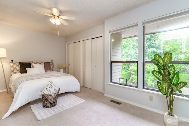 carpeted bedroom with multiple windows, a textured ceiling, multiple closets, and ceiling fan