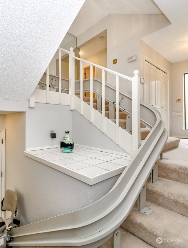 stairway with a textured ceiling and carpet floors