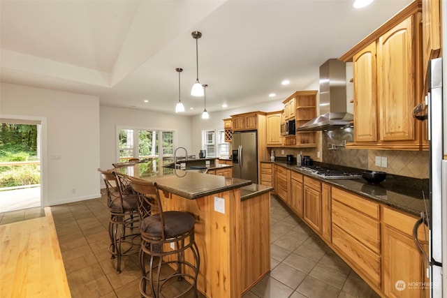 kitchen with recessed lighting, stainless steel appliances, wall chimney range hood, a large island, and backsplash