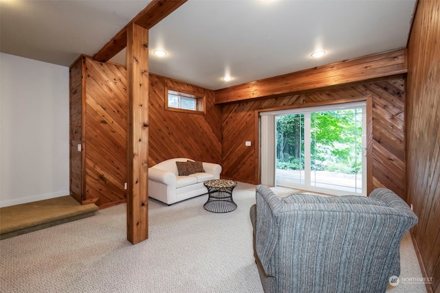 carpeted living area with beam ceiling, wooden walls, and baseboards