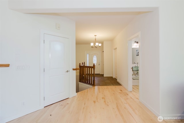 entryway with baseboards, a chandelier, and wood finished floors