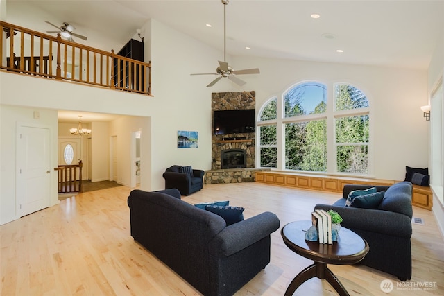 living area featuring ceiling fan with notable chandelier, high vaulted ceiling, a stone fireplace, and wood finished floors