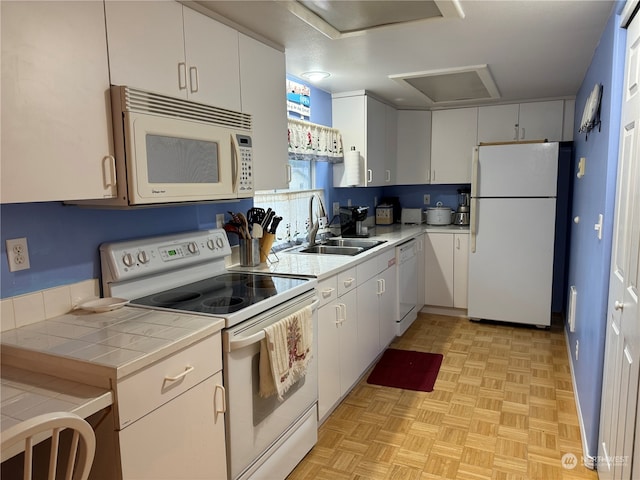 kitchen with light parquet floors, white appliances, tile countertops, sink, and white cabinetry