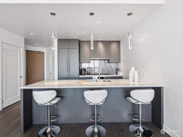 kitchen with backsplash, light countertops, gray cabinets, a kitchen breakfast bar, and a sink