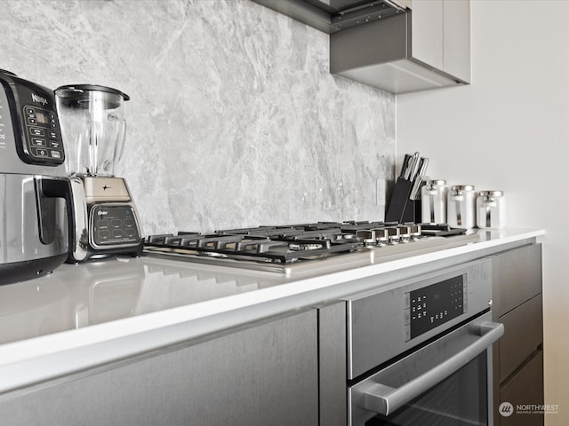 interior details featuring decorative backsplash, gray cabinets, and stainless steel oven