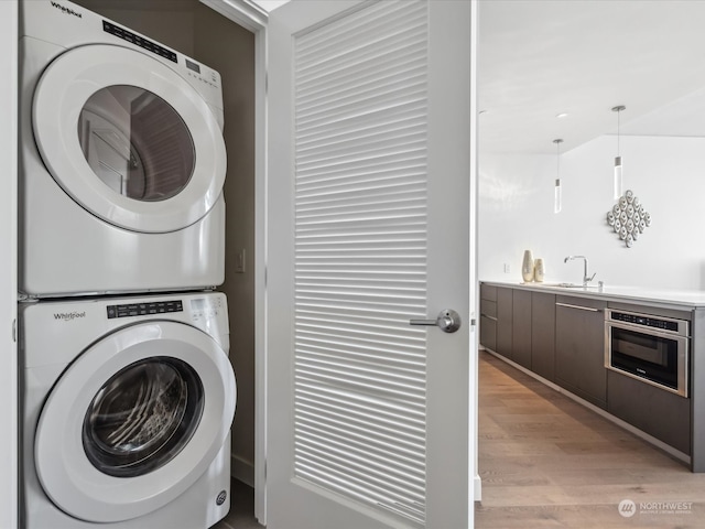 laundry area featuring light wood-type flooring, stacked washer / dryer, and sink