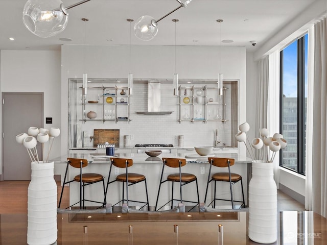 kitchen featuring wall chimney range hood, wood finished floors, backsplash, and stainless steel gas cooktop