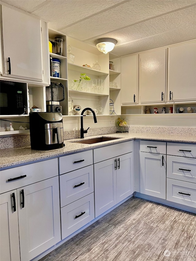 kitchen featuring sink, light wood-type flooring, black microwave, light stone countertops, and white cabinetry