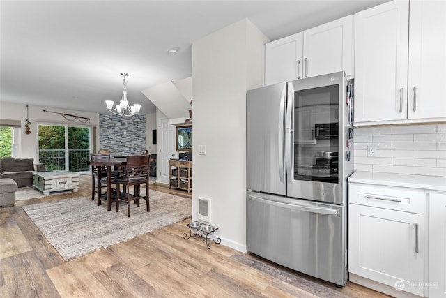 kitchen featuring light wood-type flooring, tasteful backsplash, white cabinets, stainless steel refrigerator, and a notable chandelier