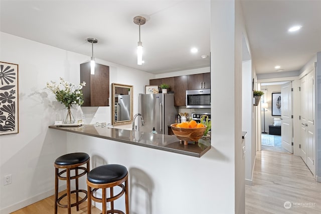 kitchen featuring appliances with stainless steel finishes, a kitchen bar, dark brown cabinetry, light wood-type flooring, and kitchen peninsula