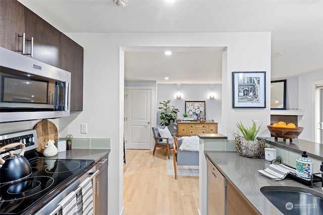 kitchen with appliances with stainless steel finishes, sink, light hardwood / wood-style flooring, and dark brown cabinets