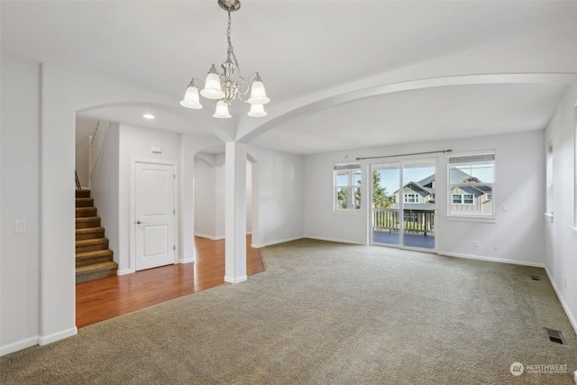 empty room with visible vents, arched walkways, stairway, an inviting chandelier, and carpet flooring