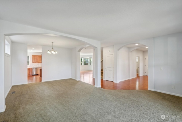 unfurnished living room with arched walkways, carpet floors, visible vents, and an inviting chandelier