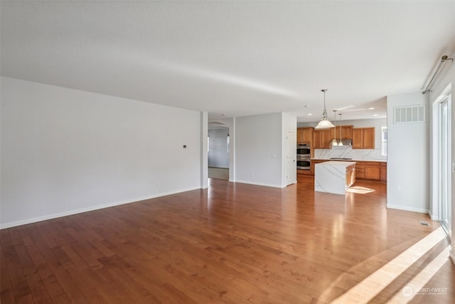 unfurnished living room featuring light wood-style flooring, visible vents, arched walkways, and baseboards