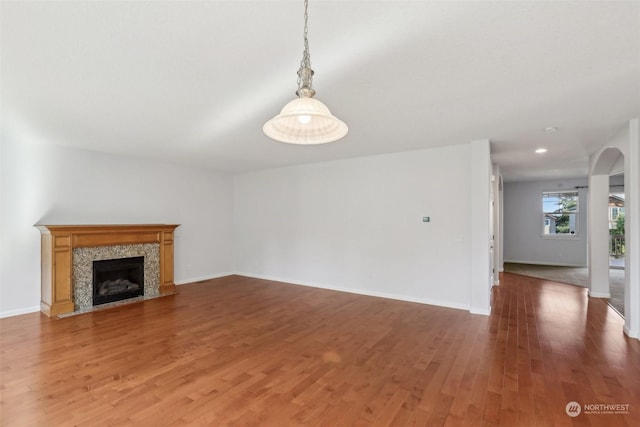 unfurnished living room featuring baseboards, arched walkways, wood finished floors, and a tile fireplace