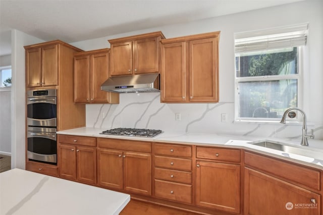 kitchen featuring appliances with stainless steel finishes, light countertops, a sink, and under cabinet range hood