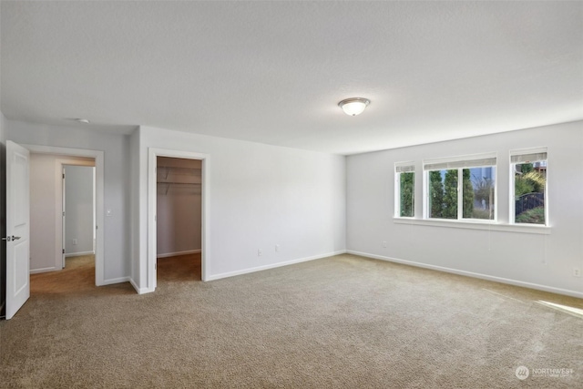 unfurnished bedroom featuring a closet, a spacious closet, baseboards, and carpet flooring