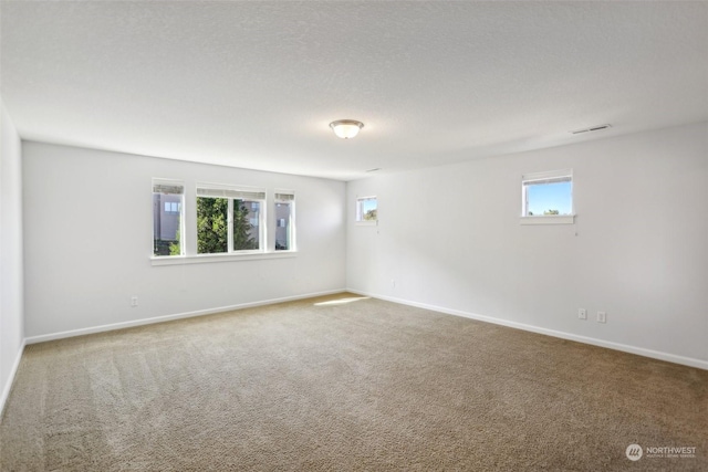 unfurnished room featuring a textured ceiling, carpet flooring, visible vents, and baseboards