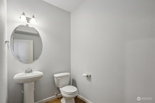 half bathroom with a sink, wood finished floors, toilet, and baseboards