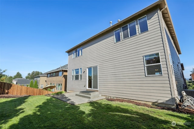 rear view of house featuring entry steps, fence, a lawn, and a patio