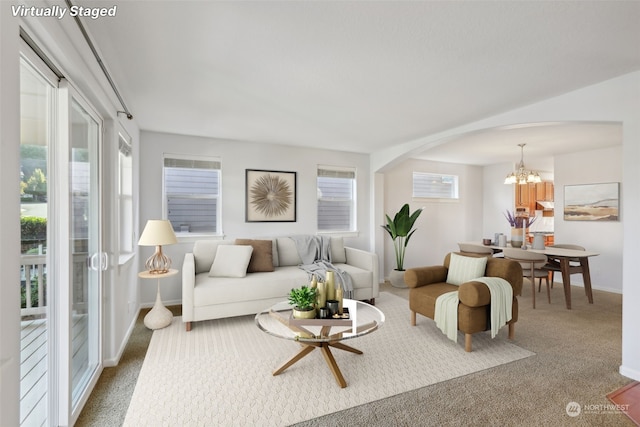 carpeted living area featuring arched walkways, baseboards, and a notable chandelier