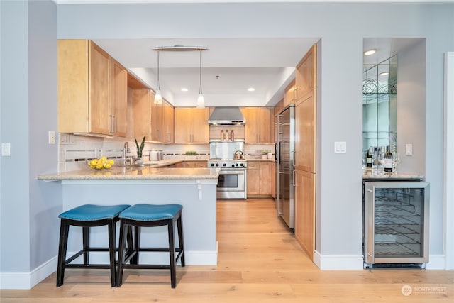 kitchen featuring decorative light fixtures, light wood-type flooring, light stone countertops, beverage cooler, and wall chimney range hood