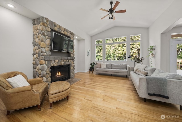 living room featuring lofted ceiling, ceiling fan, a stone fireplace, and light hardwood / wood-style floors