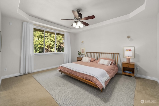 bedroom with light colored carpet, ceiling fan, and a tray ceiling