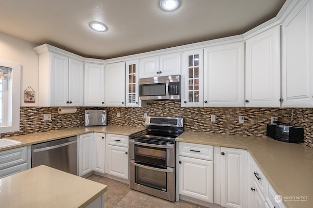 kitchen featuring appliances with stainless steel finishes, light tile patterned floors, decorative backsplash, and white cabinets