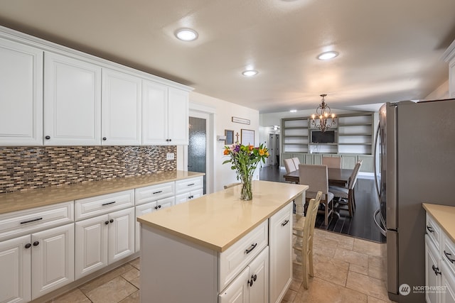 kitchen with white cabinetry, hanging light fixtures, decorative backsplash, and stainless steel fridge