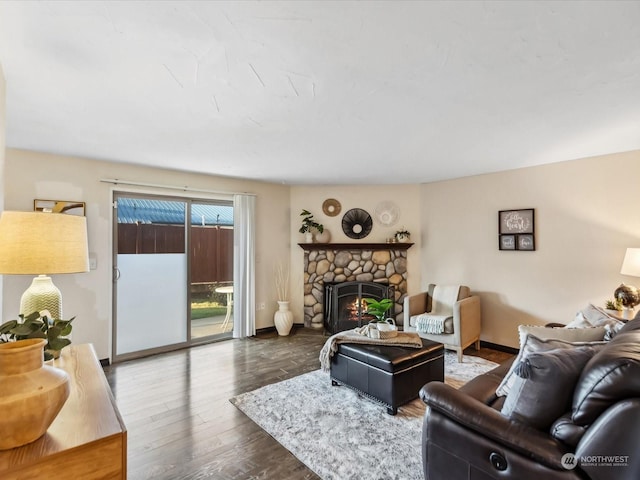 living room featuring baseboards, a stone fireplace, and wood finished floors