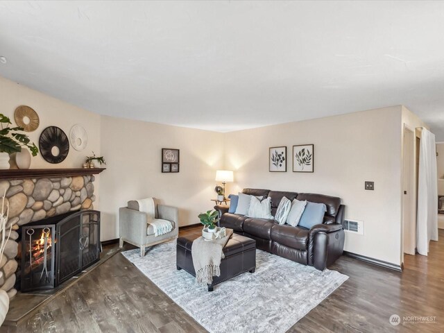 living room featuring visible vents, baseboards, a stone fireplace, and wood finished floors