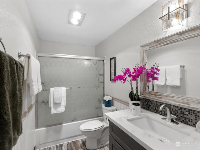 bathroom with vanity, wood finished floors, enclosed tub / shower combo, decorative backsplash, and toilet