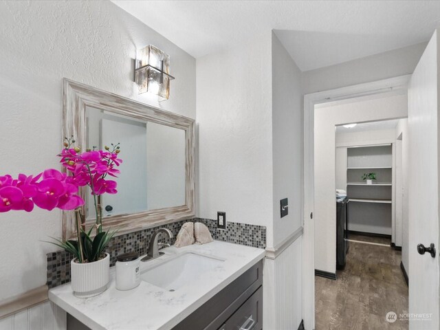 bathroom with tasteful backsplash, vanity, a textured wall, and wood finished floors