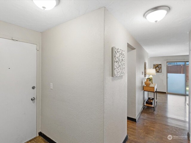 corridor featuring a textured wall, baseboards, and wood finished floors