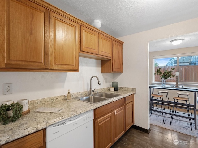 kitchen featuring brown cabinetry, white dishwasher, a sink, dark wood-type flooring, and a textured ceiling
