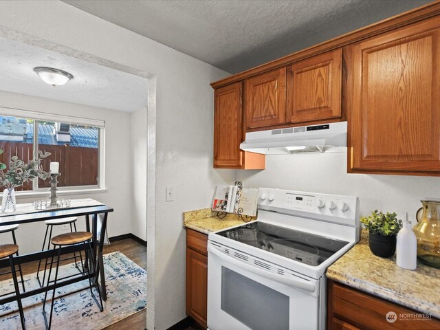kitchen featuring white range with electric cooktop, dark wood finished floors, under cabinet range hood, brown cabinetry, and a textured ceiling
