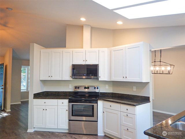 kitchen with dark wood-style floors, lofted ceiling, hanging light fixtures, appliances with stainless steel finishes, and white cabinets