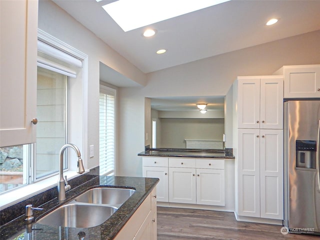 kitchen featuring dark wood finished floors, stainless steel refrigerator with ice dispenser, white cabinetry, a sink, and dark stone counters