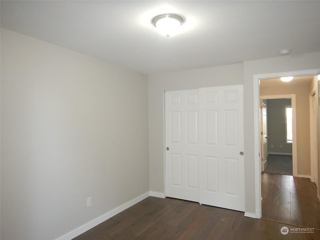 unfurnished bedroom featuring dark wood-style flooring, a closet, and baseboards